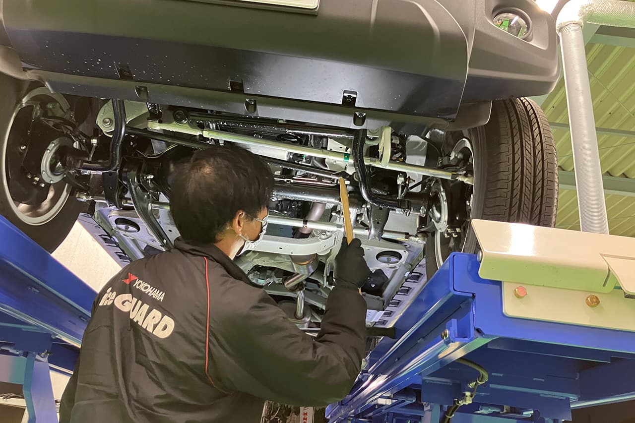 リフトで持ち上げた車の底面を点検する、整備士。